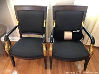 Pair of black and gold wooden armchairs with black upholstery. One chair has a bolster cushion, the other chair seat cushion missing.