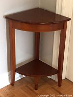 Side view of the 3-legged wooden corner table against the wall, showing leg design and overall shape