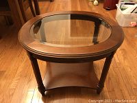 Full view of round coffee table with glass top and wooden frame, lower shelf visible.