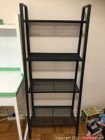 Full view of the tall black metal mesh bookshelf with four shelves, showing overall condition and size relative to surrounding objects.