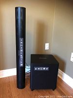 Full view of soundbar tower and subwoofer side by side on wood floor against tan wall
