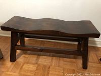 Front and side angled view of the solid wood bench showing the wave-shaped seat and sturdy legs.