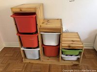 Front view of wooden stair-shaped organizer with six plastic bins in red, white, and green, showing three step levels.