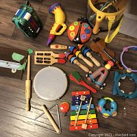 Photo showing all various baby to children's music toys and instruments spread on the floor including painted wooden and plastic percussion instruments, toy guitars, small tambourines and maracas.