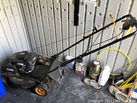 Side view of the Poulan Pro lawnmower showing the engine, wheels, and handle, with various other garage/storage items around it.