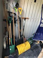 Photo showing garden tools including shovels, rake, snow shovel, leaf vacuum, and other tools stored together.