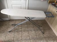 White ironing board with metal legs and iron rest on tiled floor