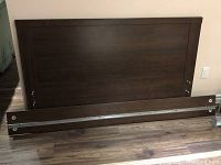 Headboard with attached metal support rail and footboard laid on floor showing wood grain and dark brown finish