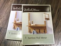 Two boxed WholeHome bamboo wall mirrors on wood floor, showing product image and brand.