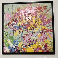 Full view of the abstract expressionist oil painting showing bright multi-color splashes and drips on a light background, framed in black wood.