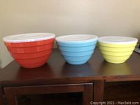Front view of the three mixing bowls with their white lids on, showing red, blue and yellow colors and ribbed design.