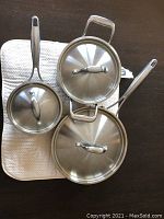 Top view of three pieces of cookware: large and small saucepan with lids and frying pan with lid.
