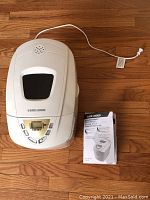 White Black & Decker bread maker with top lid window and digital buttons next to instruction manual.