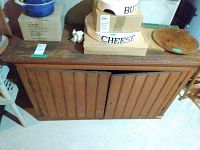 Photo showing entire wood cabinet with two doors, vertical paneling, and the top surface with some boxes and items placed on it.