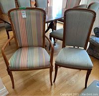 Pair of dining chairs shown: one armchair with wood veneer frame and striped upholstery, one side chair matching upholstery, both with some wear.