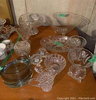 Overview photo of crystal and glass items on the table showing bowls, vases, creamer, and two mini clocks.