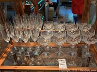 Set of 16 cut crystal glasses arranged on a mirrored surface: 8 flute glasses at left and 8 coupe glasses at right, showing overall condition and style.