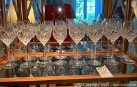 Front view of all 16 crystal wine glasses arranged on mirrored surface, showing detailed cut patterns.