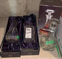Three glass decanters in original boxes arranged side-by-side on a shelf, showing each decanter and partially visible packaging