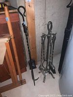 Full view of the metal fireplace tool set with stand and individual tools leaning against a wall.