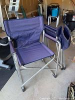 Open blue fabric folding chair with silver metal frame and fabric wrapped armrests.