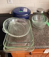 Blue Le Creuset Dutch oven with lid, Pyrex glass baking and mixing dishes, metal canister displayed on countertop.