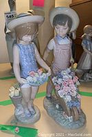 Two Lladro figurines: a girl holding a basket of flowers and a boy pushing a wheelbarrow full of flowers