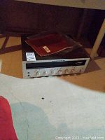 Receiver placed on concrete floor with original manual resting on top, displaying entire unit and wooden case cover