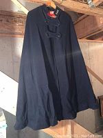 Full view of navy blue nurses cape hanging on wooden hanger in basement setting.