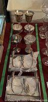 Top view of 2 large and 6 small silverplate wine goblets together with 2 candle holders and 2 snuffers on a table.