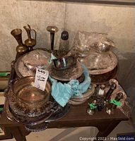 Photo showing multiple tarnished silverplate serving pieces stacked together on a wooden surface against a stone wall background, including bowls, trays, and candle holders.