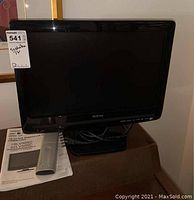 Front view of Toshiba 19LV505C LCD TV on stand with remote and manual beside it