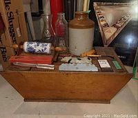 Photo showing wood seed box base with multiple vintage items on top including pottery crock, glass bottles, and kitchen tools.