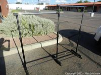 Single black metal light-duty clothing rack with one horizontal hanging rod, adjustable frame, and wheels on the base shown outside.
