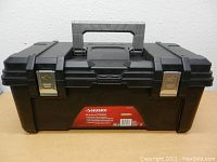 Front view of black Husky 26 inch toolbox with metal latches and central handle, label visible on front, showing overall condition and crack presence.