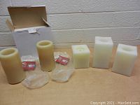 Lot of five LED light wax candles, three square white and two beige cylindrical, with remote controls and original packaging.