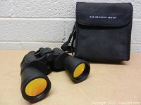Front view of the Sharper Image binoculars with orange-tinted lenses and black carrying case behind.