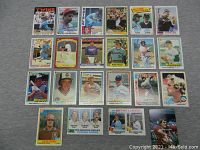 Top-down view of 23 vintage baseball cards spread out on a grey fabric surface, showing front faces of the cards including players like Pete Rose, Carl Yastrzemski, and others.
