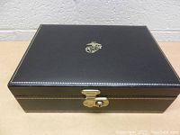 Closed black box with gold Marine Corps emblem on lid, gold detailing on edges, lock at front.
