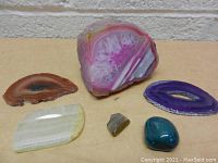 Five polished rock and geode pieces on a wooden surface, showing their colors and patterns
