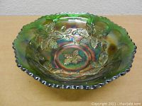 Top-down view showing detailed embossed leaves and the iridescent green finish of the carnival glass bowl with scalloped edge.