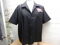 Front and front-side angle views of the black Arizona Cardinals bowling shirt, showing logo, buttons, collar, and piping detail.