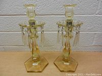 Front view of a pair of vintage amber glass candlesticks with hexagonal bases and dangling clear glass crystal prisms.