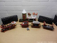 Full overview of the Christmas train set with all train cars, track pieces, and decorative components arranged on a white brick wall floor surface.