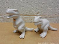 Pair of white ceramic T-Rex dinosaur salt and pepper shakers, one with open mouth and the other with closed mouth, seen from front angle.