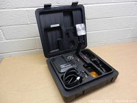 Photo showing opened black plastic case with 200 PSI compressor, pressure gauge, and emergency light with adjustable arm inside compartments
