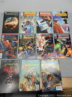 Photo showing eleven assorted comic books in two rows on a gray surface, titles include DC Universe, Warrior, Excalibur, Doom 2099, Warstrike and Gen13