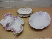 View of three vintage porcelain dishes including a divided tray, a lidded serving dish, and a bowl with scalloped edges on a wooden surface.