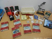 Photo showing assorted boxed and unboxed Christmas ornaments including Danbury Mint village lighted figurines, glass ball ornaments, metal candle holder, fabric basket, and small decorative holiday figurines.