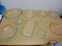 Top view of assorted clear glass kitchen dishes including bowls and rectangular baking dish on wood table.